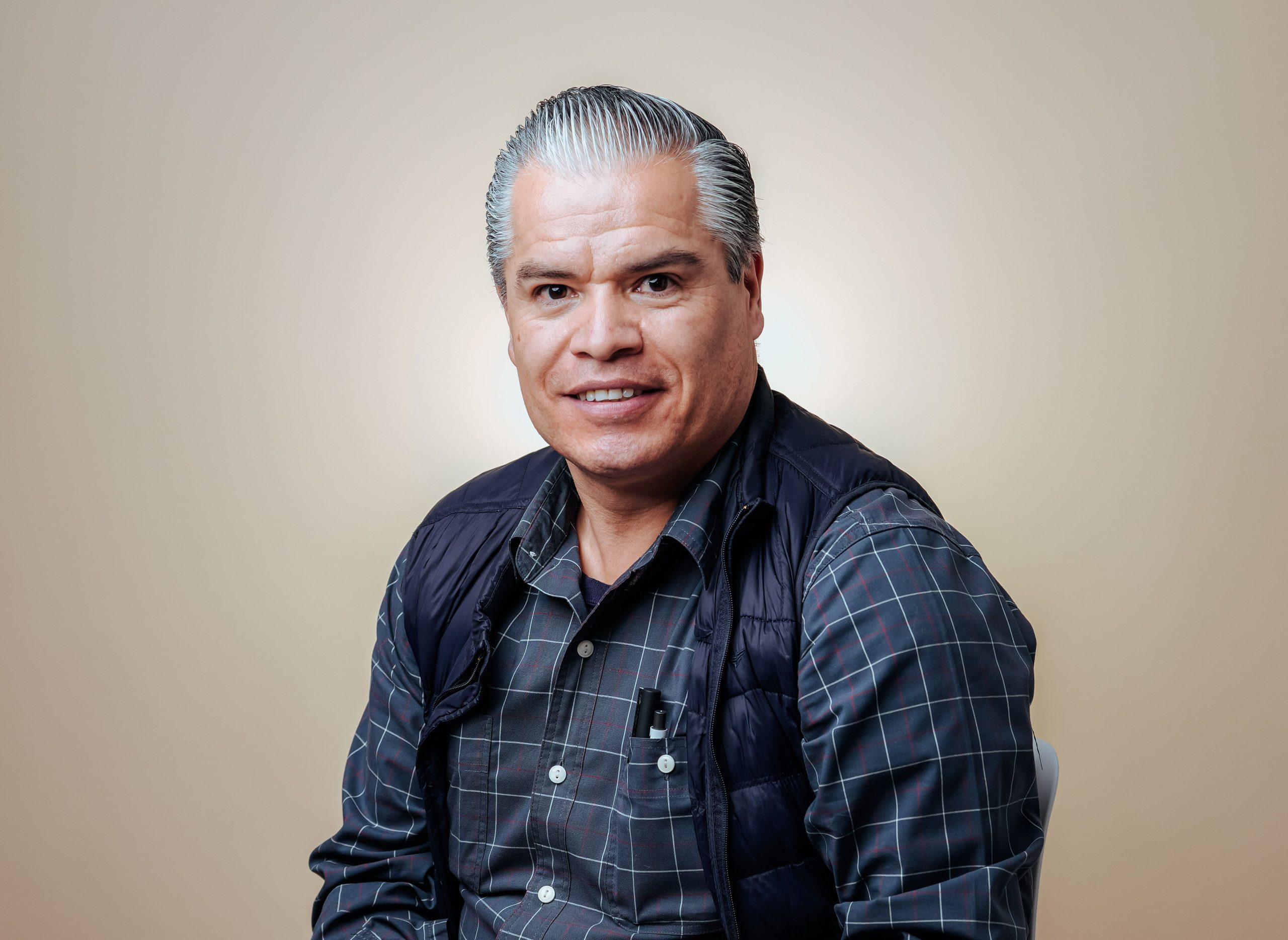 Studio portrait of a smiling mature man in a checkered shirt and vest.