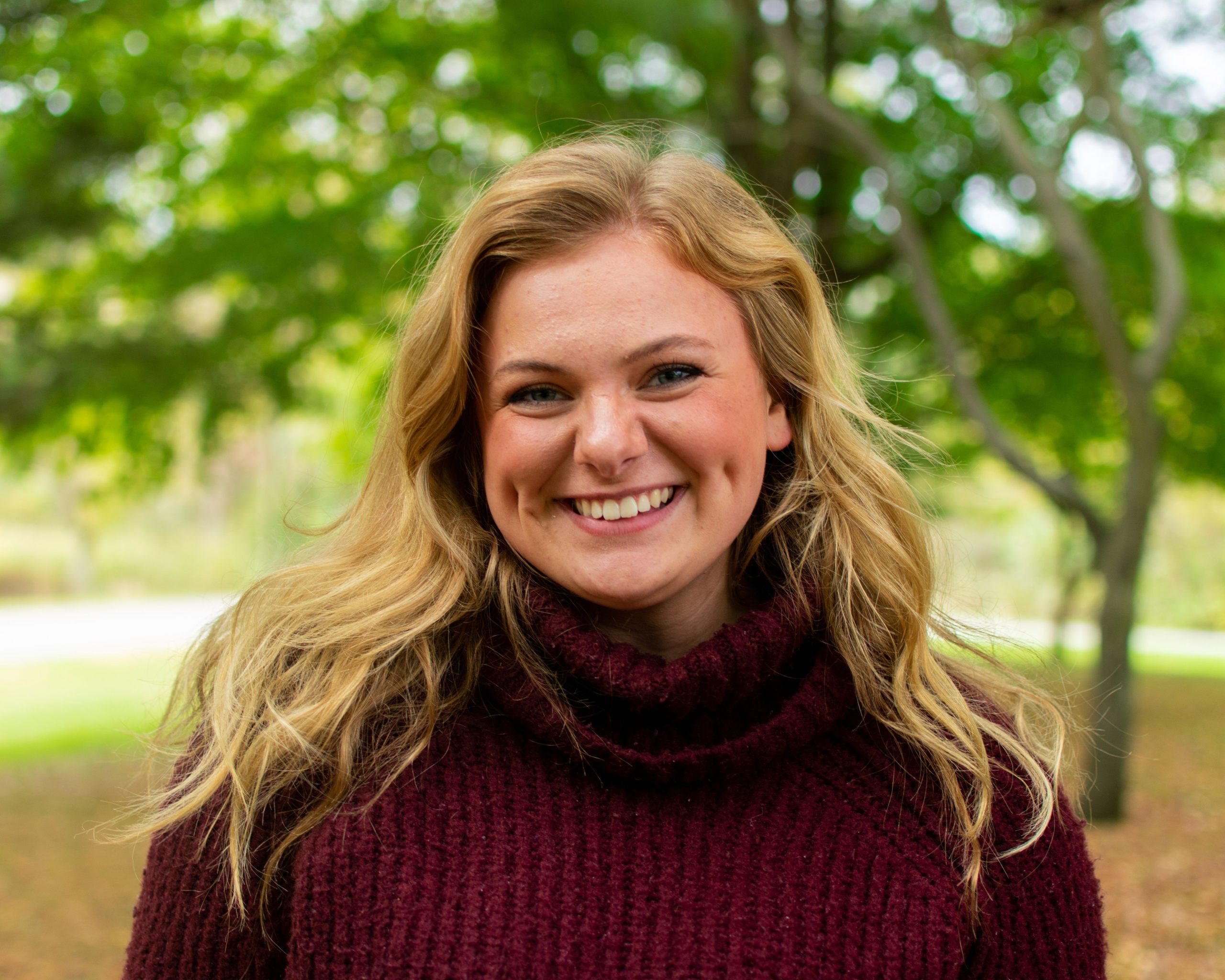 Portrait of a smiling woman with blond hair in an autumn outdoor setting.