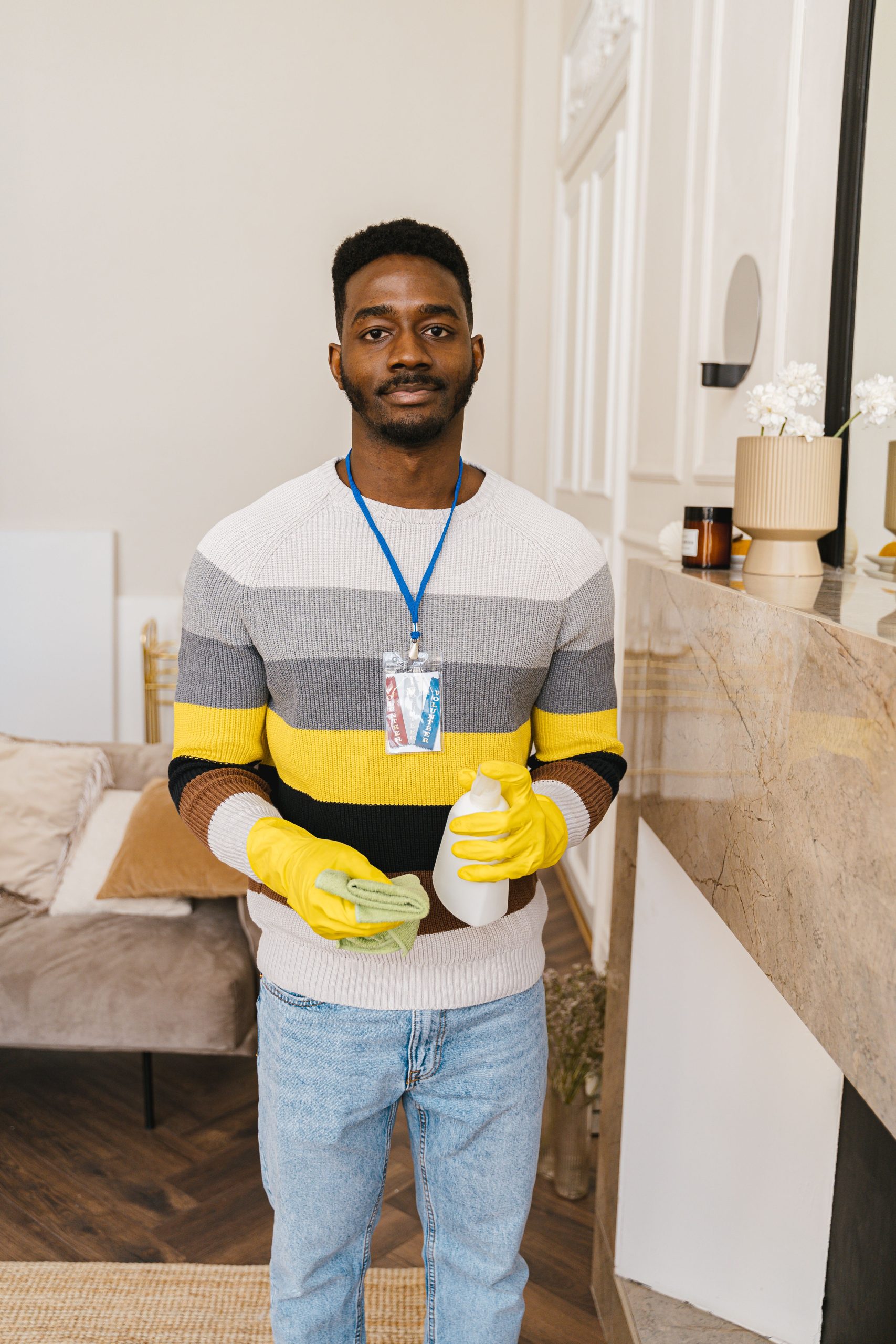 Young man volunteering, holding cleaning supplies in a modern indoor space.