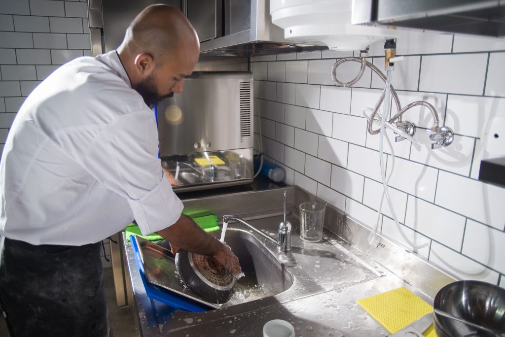 A chef cleans kitchen utensils in a stainless steel sink, maintaining hygiene standards.
